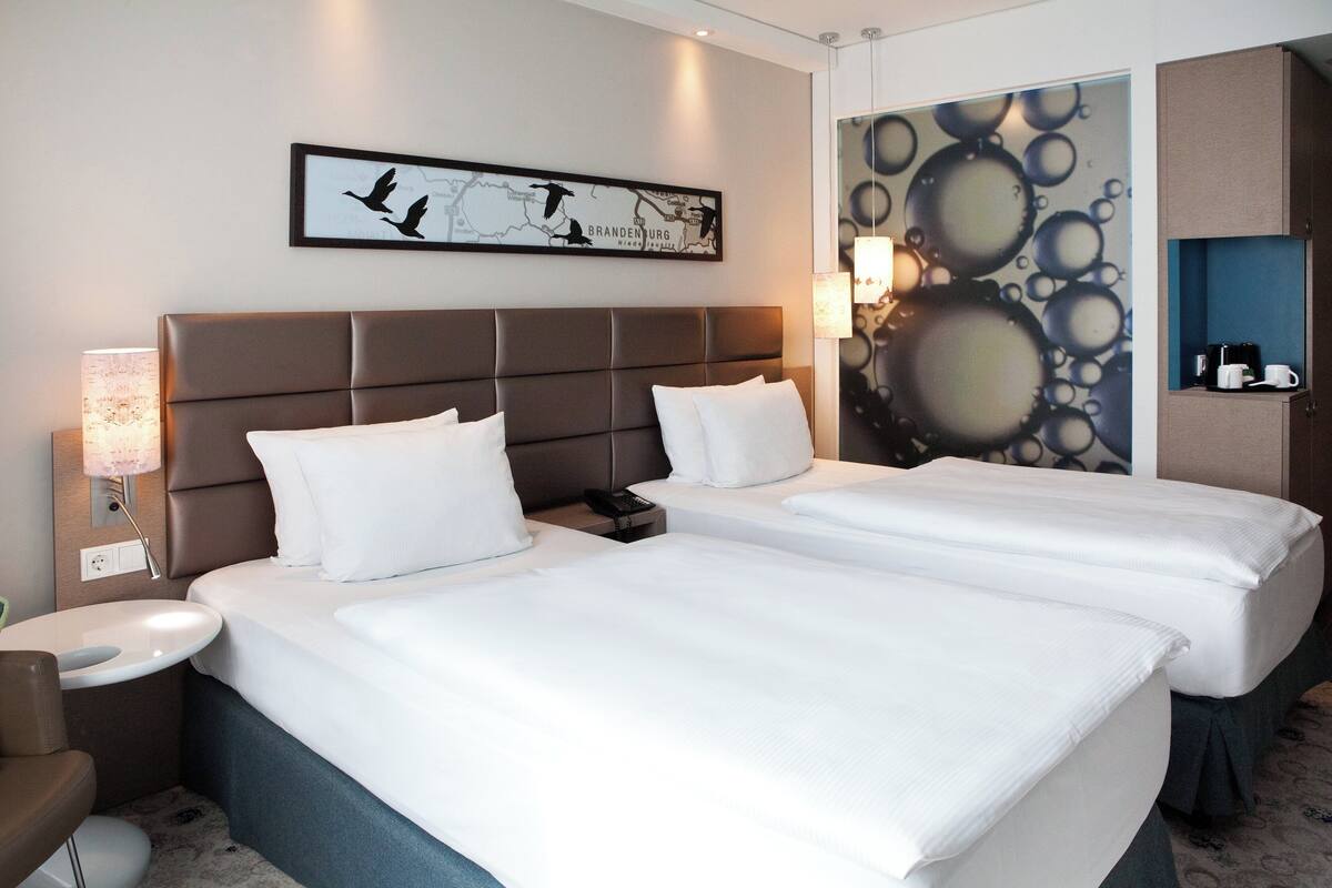 Habitación de hotel con dos camas, una mesita de noche, una lámpara, un mapa en la pared y una cafetera.