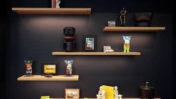 Una exhibición de objetos variados sobre estantes y una mesa, incluyendo un cuadro enmarcado de Berlín, un florero colorido y una pequeña figurita.