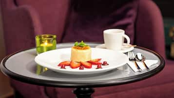 A dessert on a white plate with strawberries and a candle on a table.