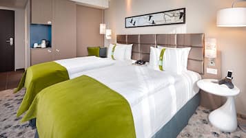 Una habitación de hotel con dos camas, una mesita de noche con un teléfono, una obra de arte en la pared y una cafetera en un rincón.