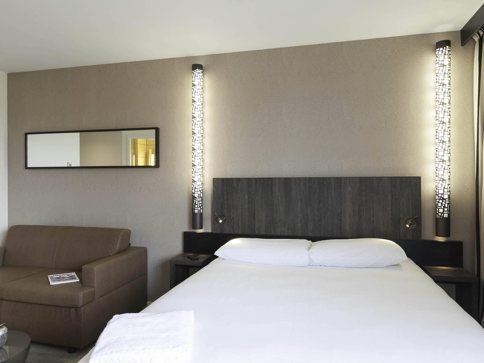 Ein Hotelzimmer mit Bett, Stuhl, Nachttisch, Spiegel und Wandleuchten.