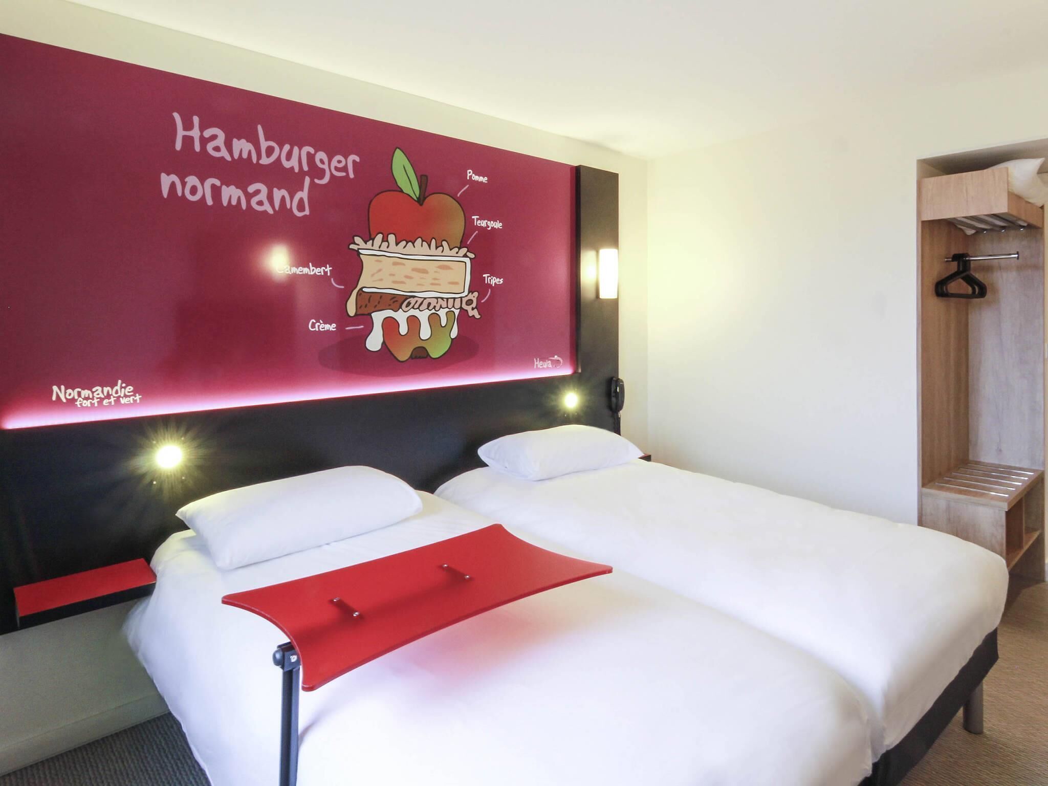 Ein Hotelzimmer mit Bett, einer roten Wand mit einer Illustration von Essen, einem Telefon und einer Holzbank.