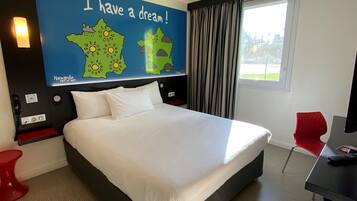 Une chambre d’hôtel avec un grand lit, un bureau, une chaise rouge, une carte accrochée au mur et une fenêtre avec des rideaux.