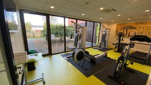 A gym with exercise equipment, large windows, and a view of the outside. - Ibis Styles Flers (Flers)