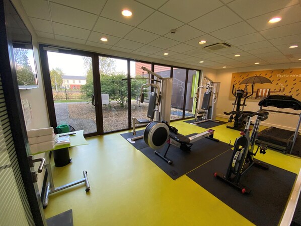 A gym with exercise equipment, large windows, and a view of the outside. - Ibis Styles Flers (Flers)