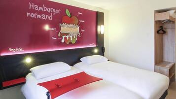 A hotel room with a large wall mural of a hamburger, a bed with white linens, and a red bedside table.