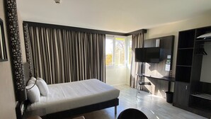 A modern hotel room with a bed, a sofa, a TV, and a dining area. - Ibis Styles Flers (Flers)