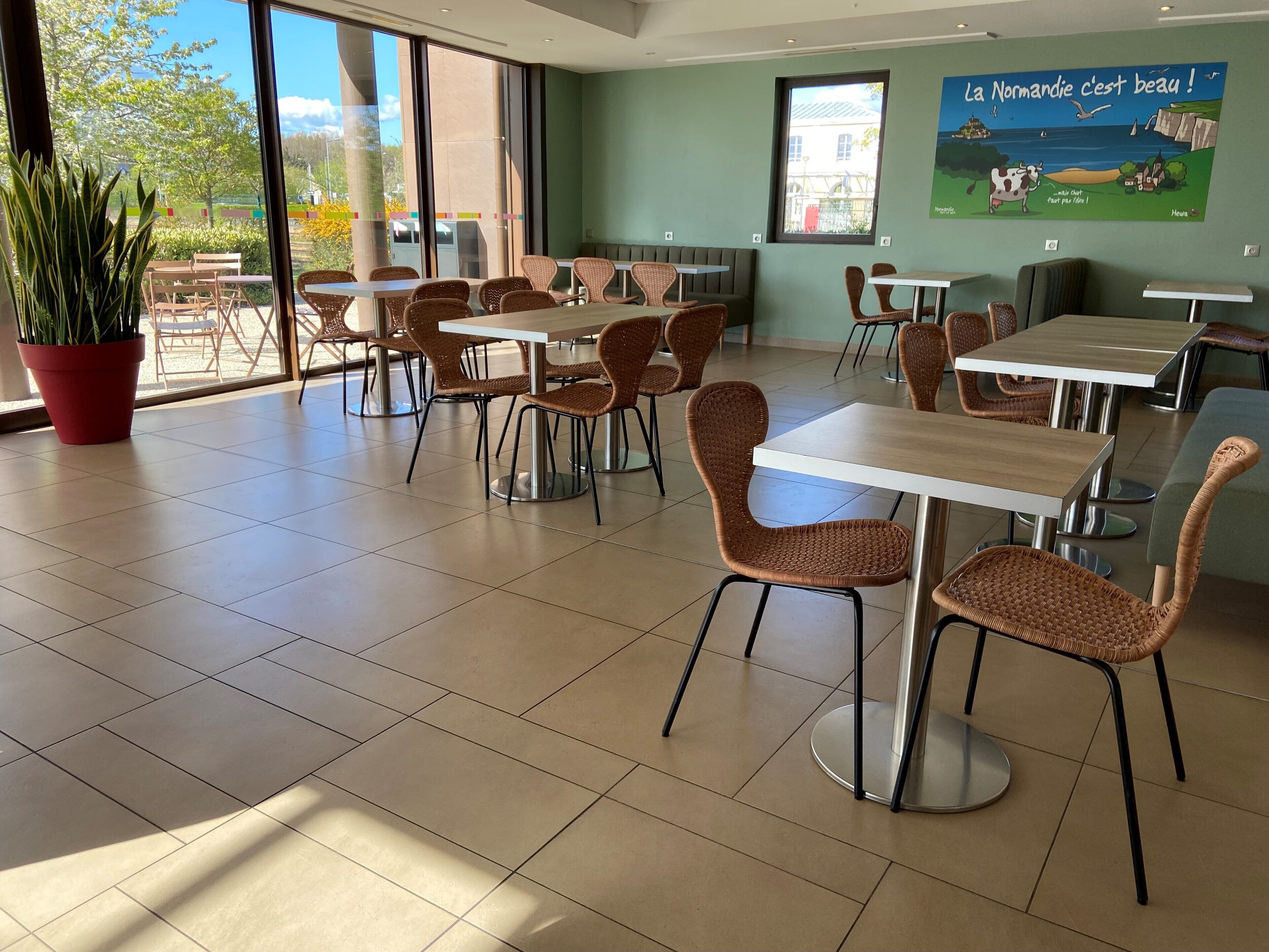 Un restaurante con sillas de mimbre, mesas blancas y ventanas amplias.