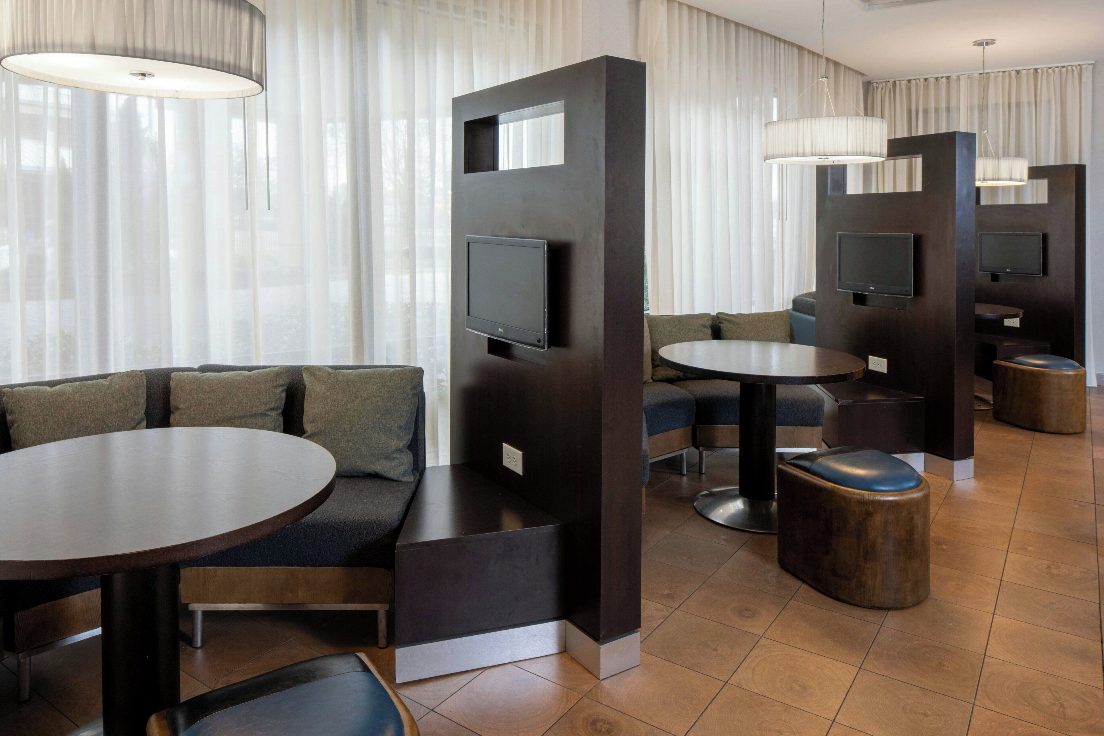 Un hall d’hôtel moderne avec un canapé modulable, des tables rondes et des écrans de télévision intégrés.
