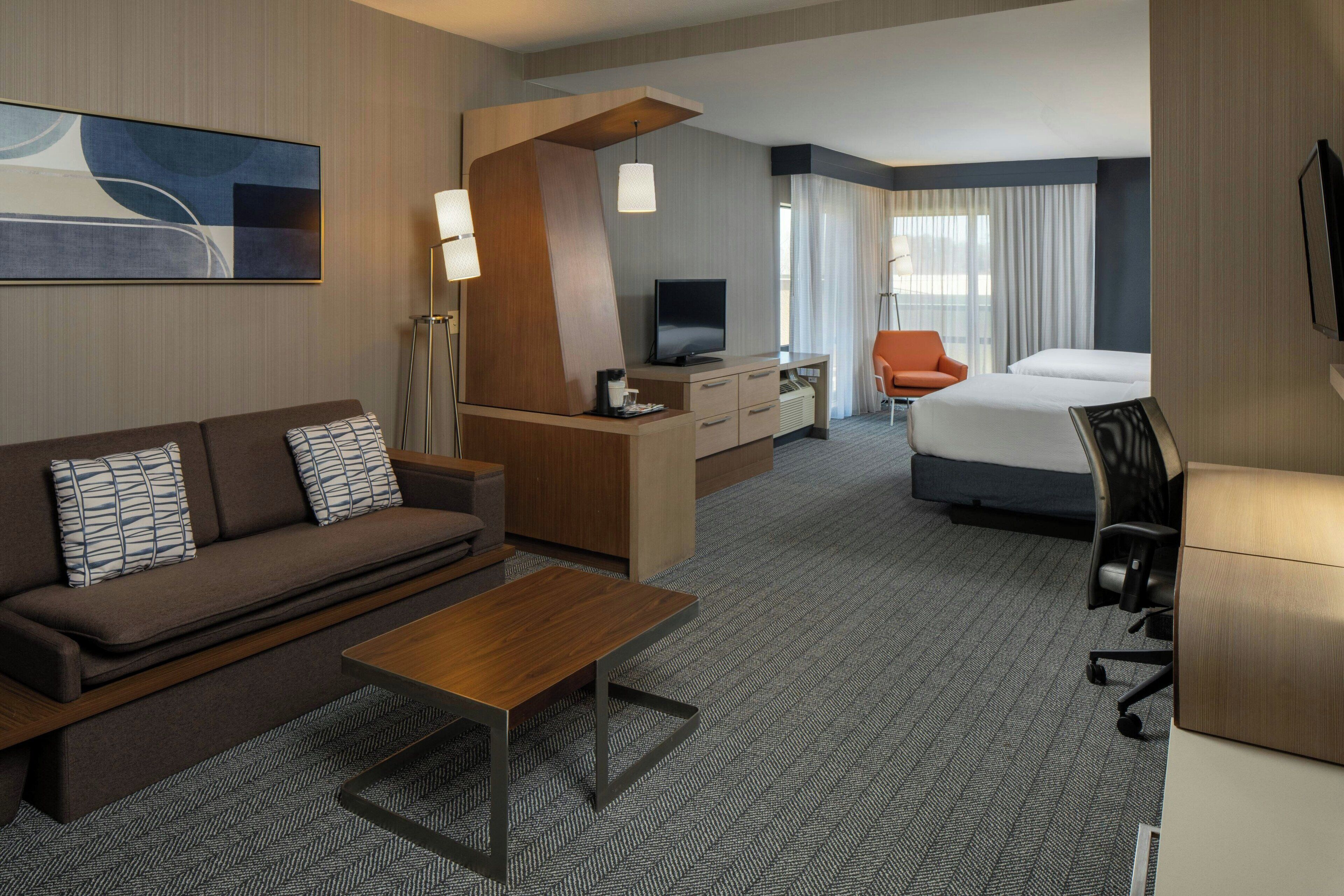 A hotel room with a sofa, a desk with a TV, a bed, and a chair.