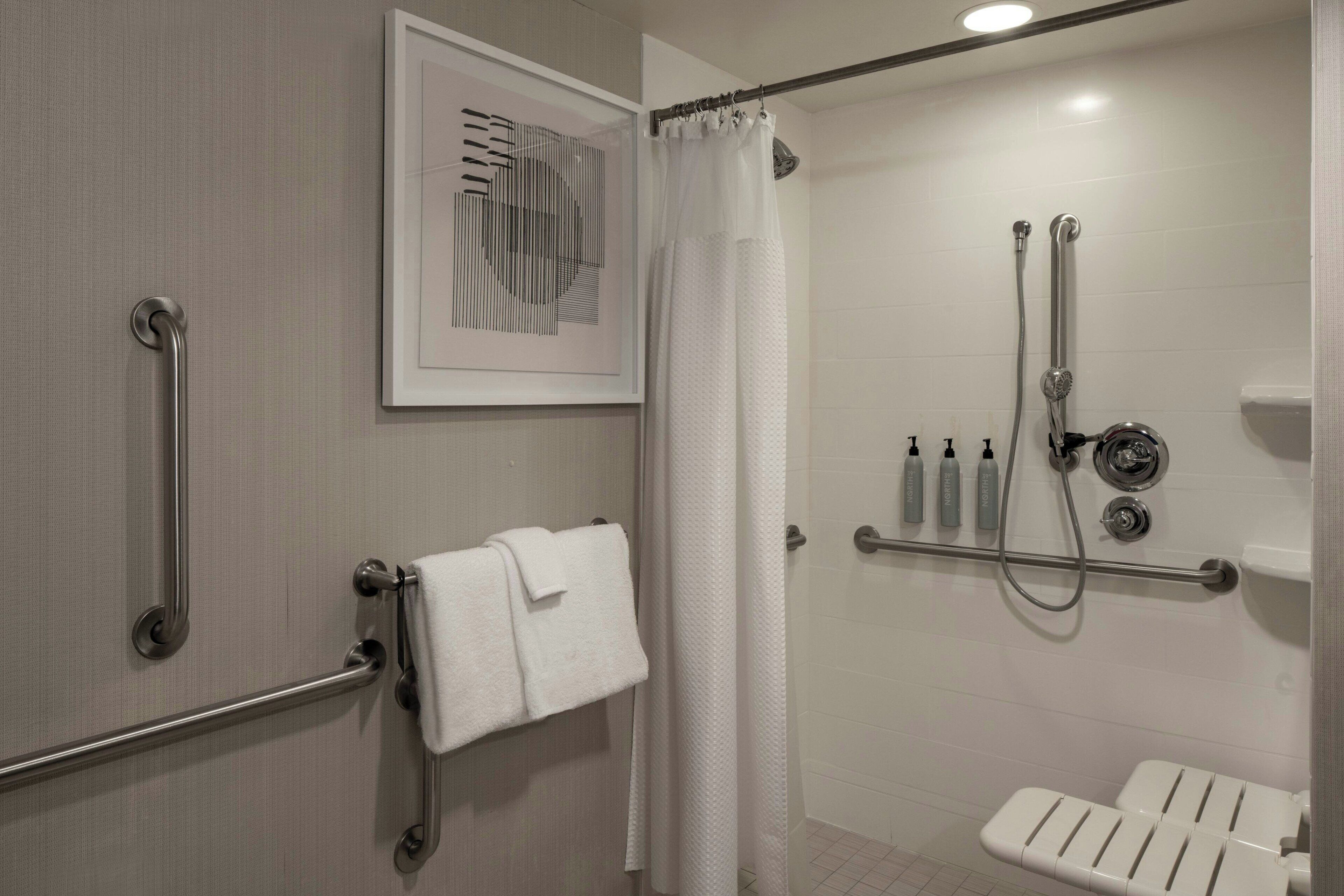 A modern bathroom with a shower, grab bars, a toilet with a safety seat, and a towel rack.