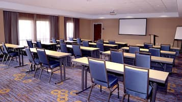 Uma sala de conferências com várias mesas e cadeiras, uma tela de projeção e um quadro branco.