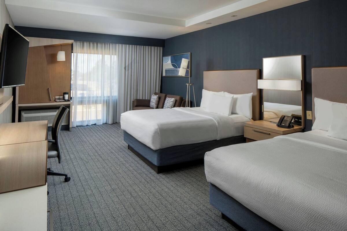 A hotel room with a large bed, a desk, a chair, a TV, and a window with curtains.