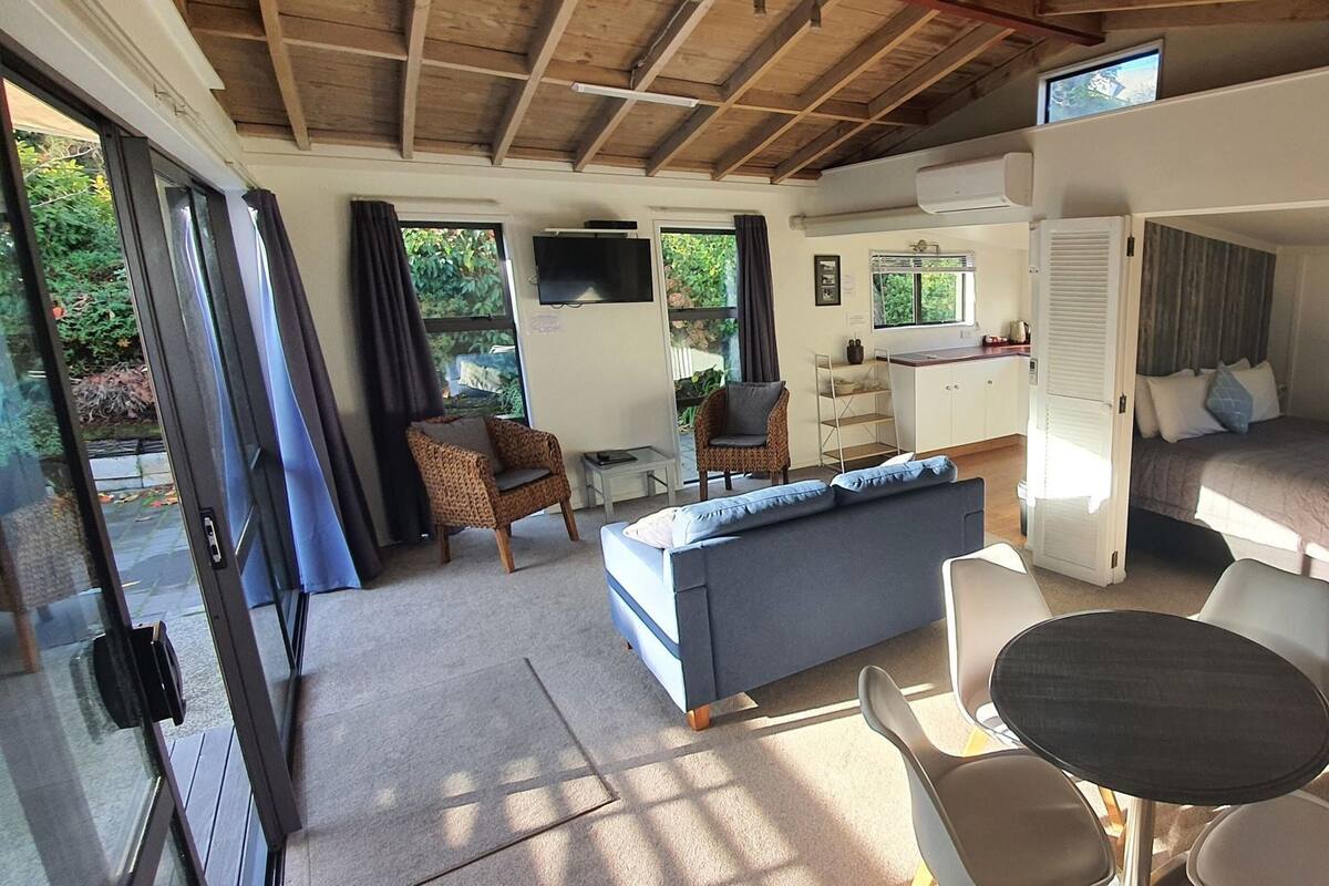 Un espacio habitable compacto y funcional con sofá, mesa de comedor y cama.