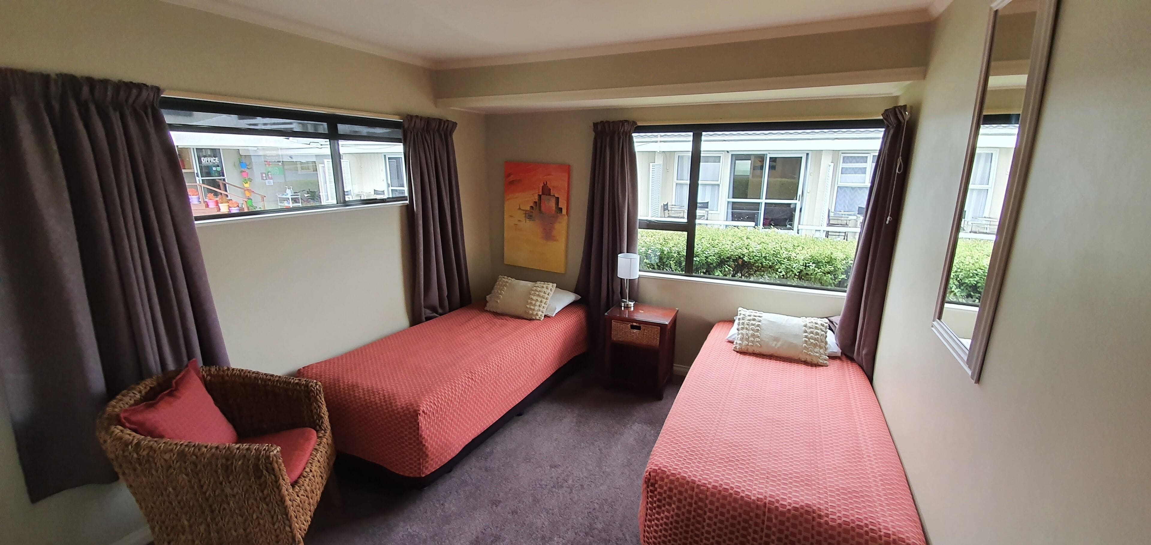 A room with two single beds, a small table, a chair, and a window with curtains.
