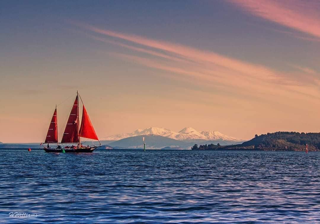 Un velero en aguas tranquilas, con montañas al fondo.