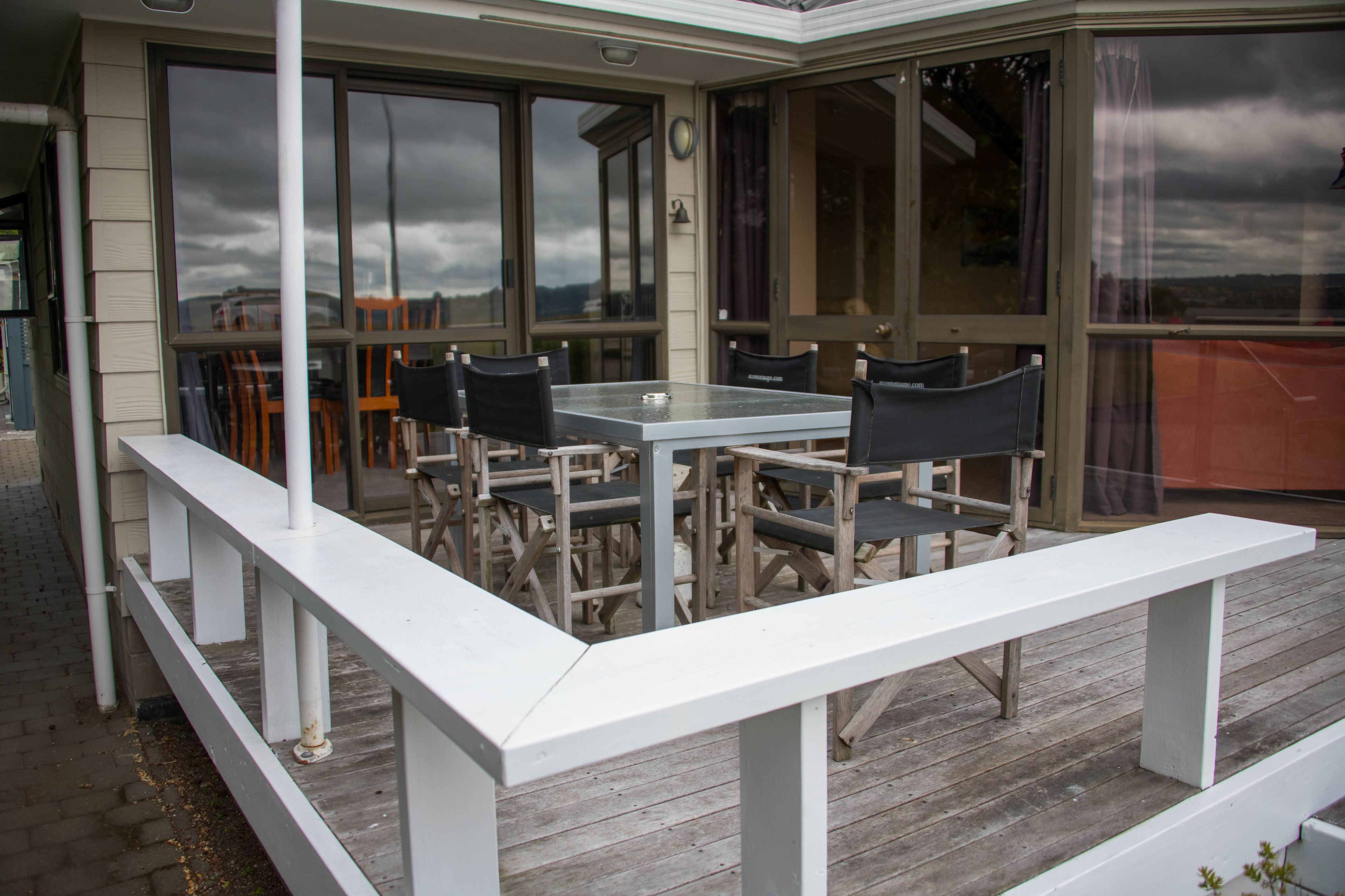 A covered outdoor seating area with a table and chairs, a white bench, and large windows.