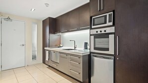 A modern kitchen with stainless steel appliances, a white countertop, and dark wooden cabinets.