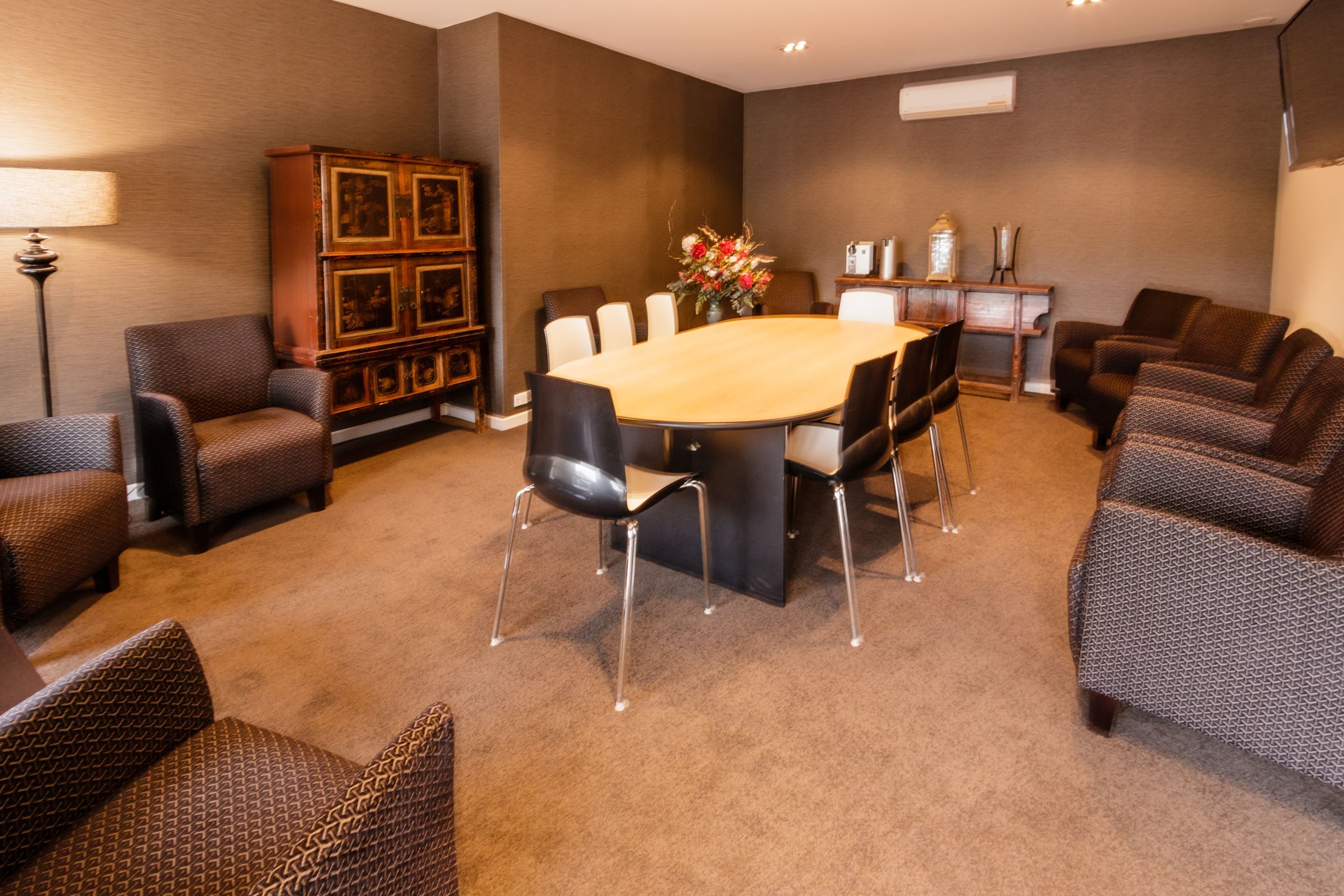 A conference room with a large table surrounded by chairs, a cabinet with framed pictures, and a vase with flowers.