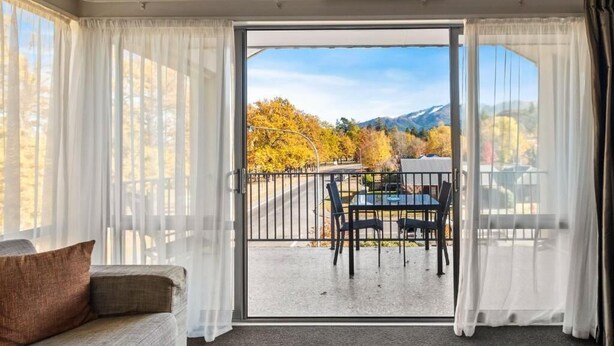 A room with a sofa, a table with chairs, and a view of a balcony with a table and chairs.