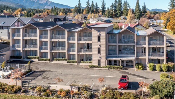 A multi-story hotel with balconies, a parking lot, and a mountainous backdrop.