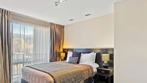 A hotel room with a large bed, two bedside tables, a view of the city, and a balcony.