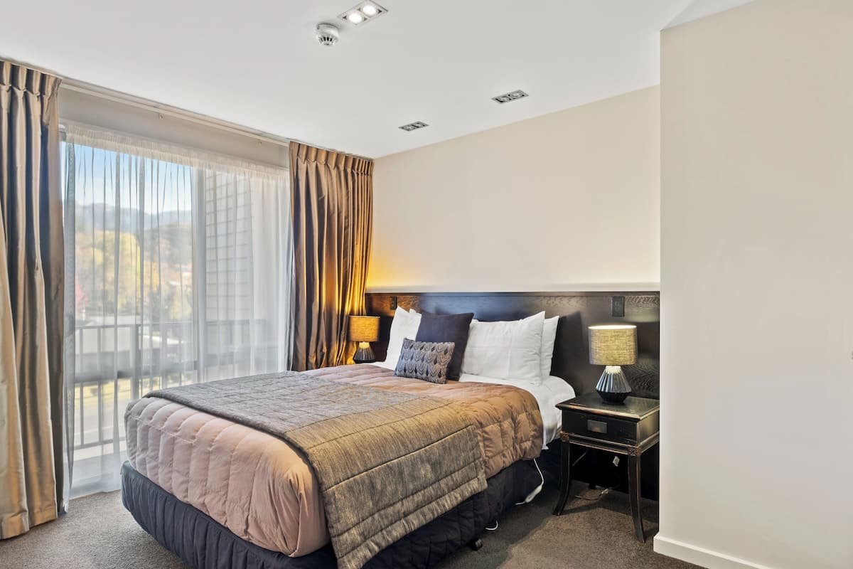 A hotel room with a large bed, two bedside tables, a view of the city, and a balcony.