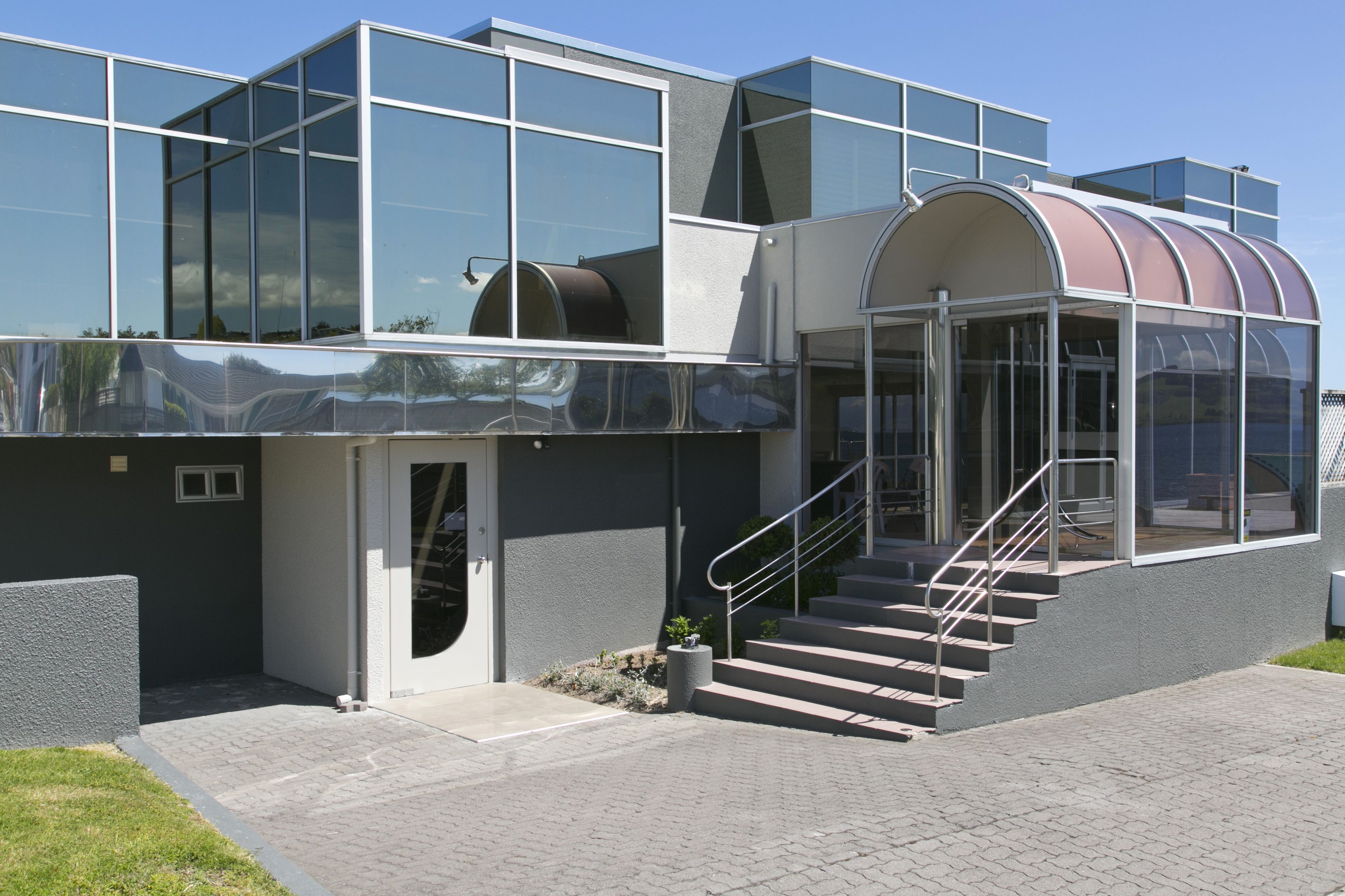 Un edificio moderno con amplios ventanales, una entrada curva de vidrio y una escalera que lleva a la entrada.