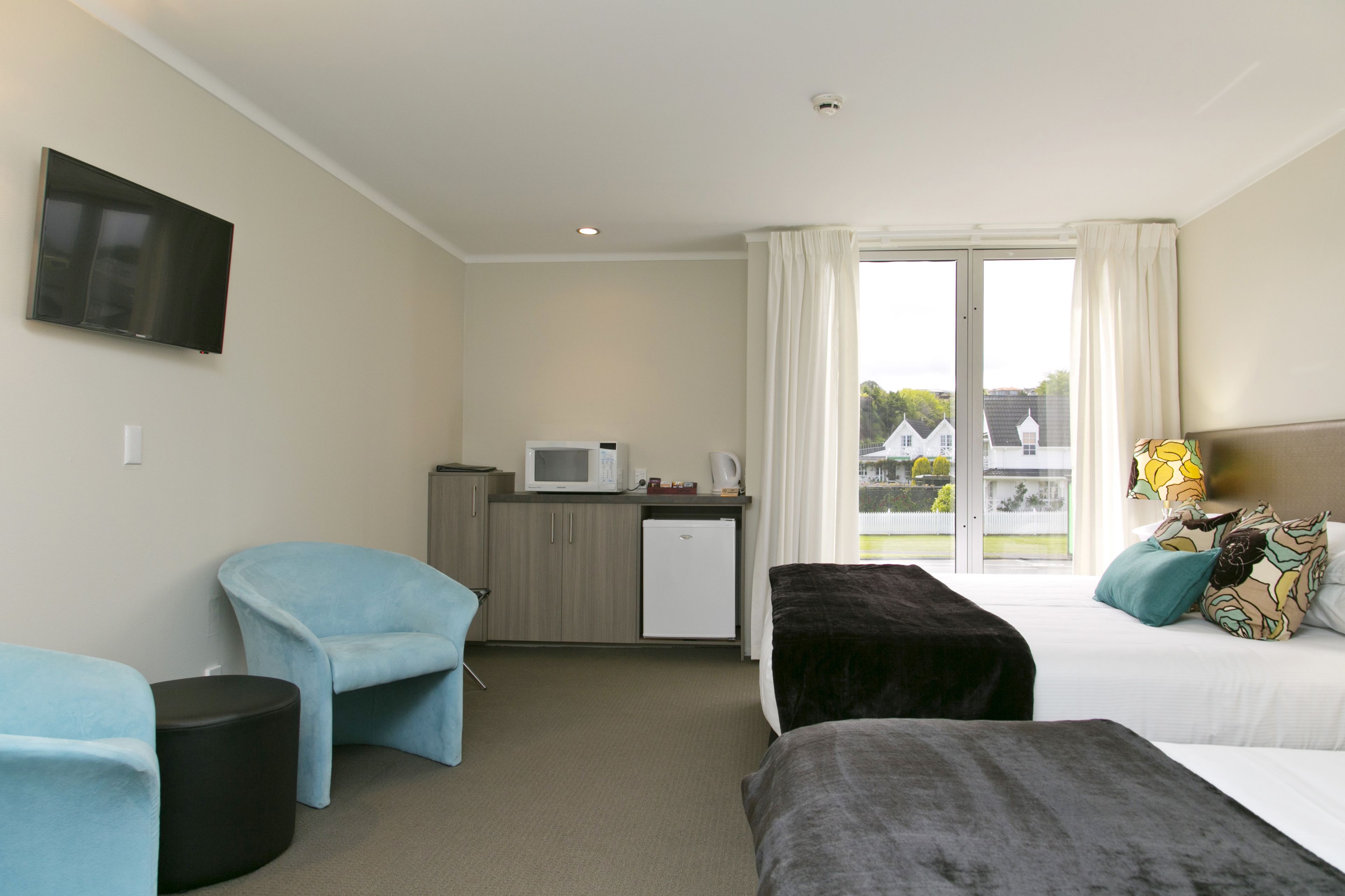 A hotel room with a bed, a desk, a chair, a TV, and a view of the outside.