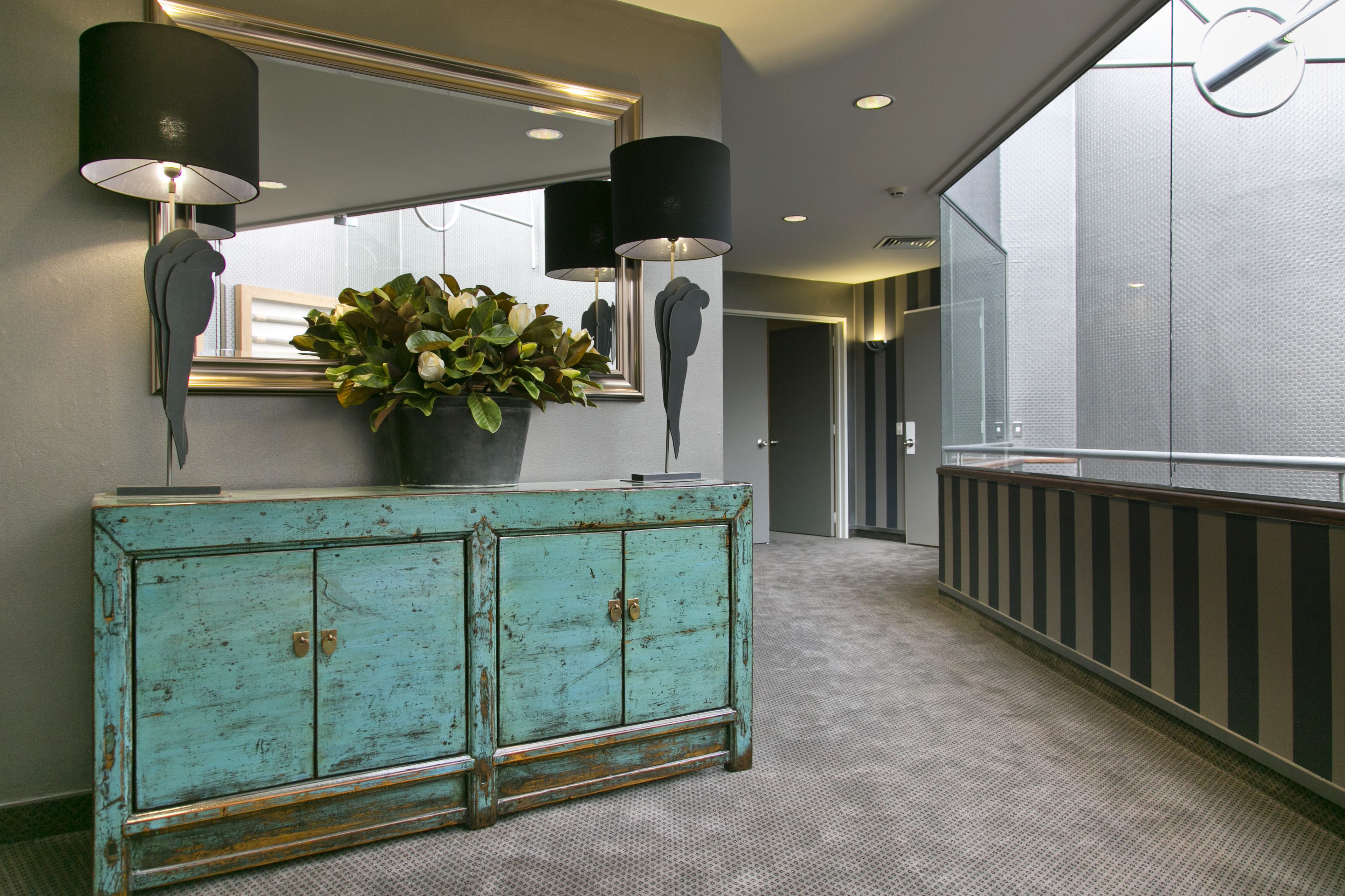 A teal-colored, distressed wooden cabinet with two doors and a large potted plant on top.