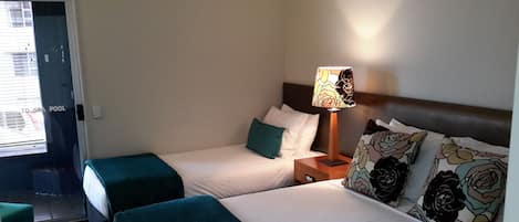 A hotel room with two single beds, a nightstand with a lamp, and a view of the spa pool.