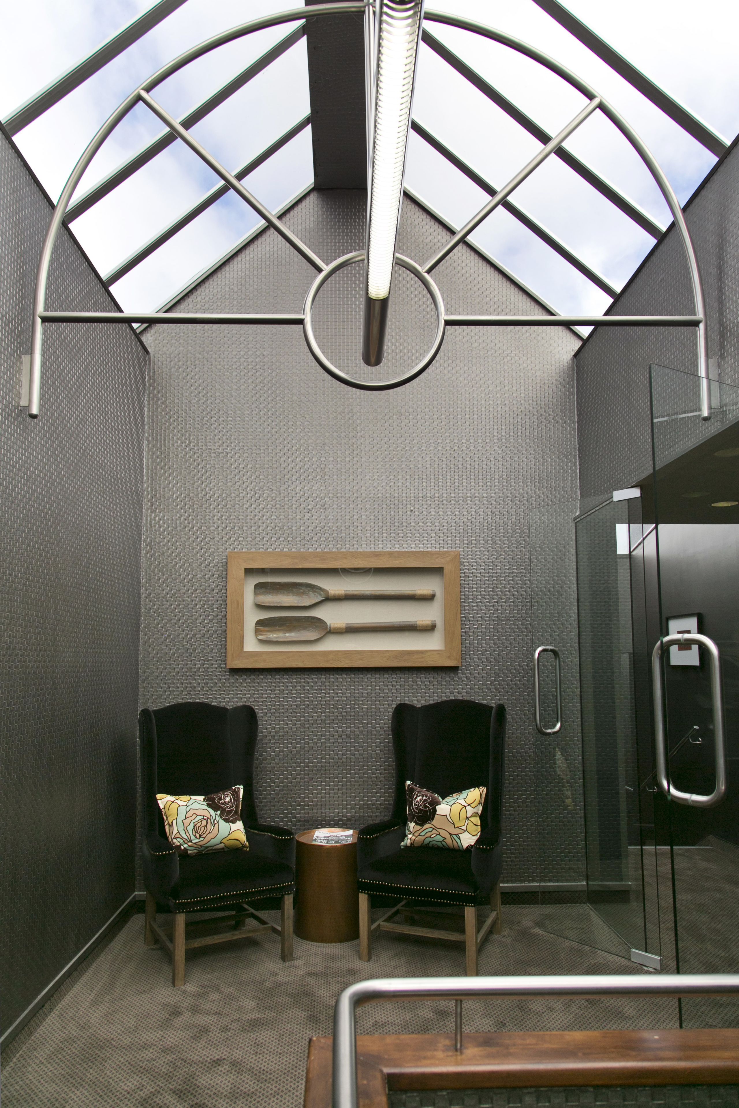 A modern waiting area with two black chairs, a small table, and a glass enclosure with a metal railing.