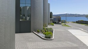 Een modern gebouw met grote cilindervormige structuren, een verhard gebied met kleine planten en uitzicht op een waterpartij.