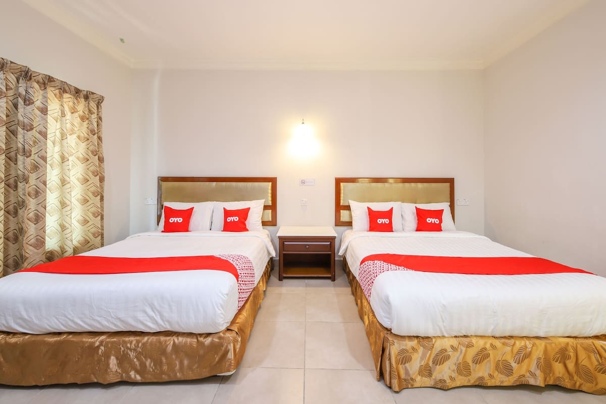Habitación de hotel con dos camas, cada una con cabecero de madera, ropa de cama blanca y almohadas rojas con la marca 'OYO'.
