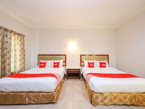 Une chambre d’hôtel avec deux lits, chacun doté d’une tête de lit en bois, de draps blancs et d’oreillers rouges portant la marque « OYO ».
