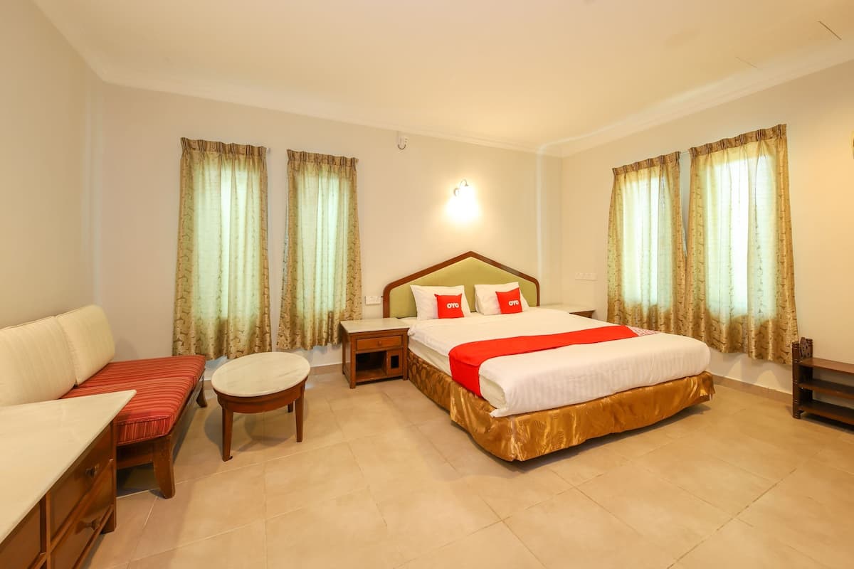 Habitación de hotel con una cama grande, una mesita pequeña, un sofá y cortinas.