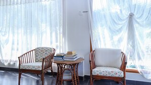 Une pièce avec deux fauteuils en osier, une petite table sur laquelle sont posés des livres et des rideaux légers.