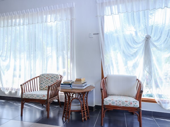 Une pièce avec deux fauteuils en osier, une petite table sur laquelle sont posés des livres et des rideaux légers.