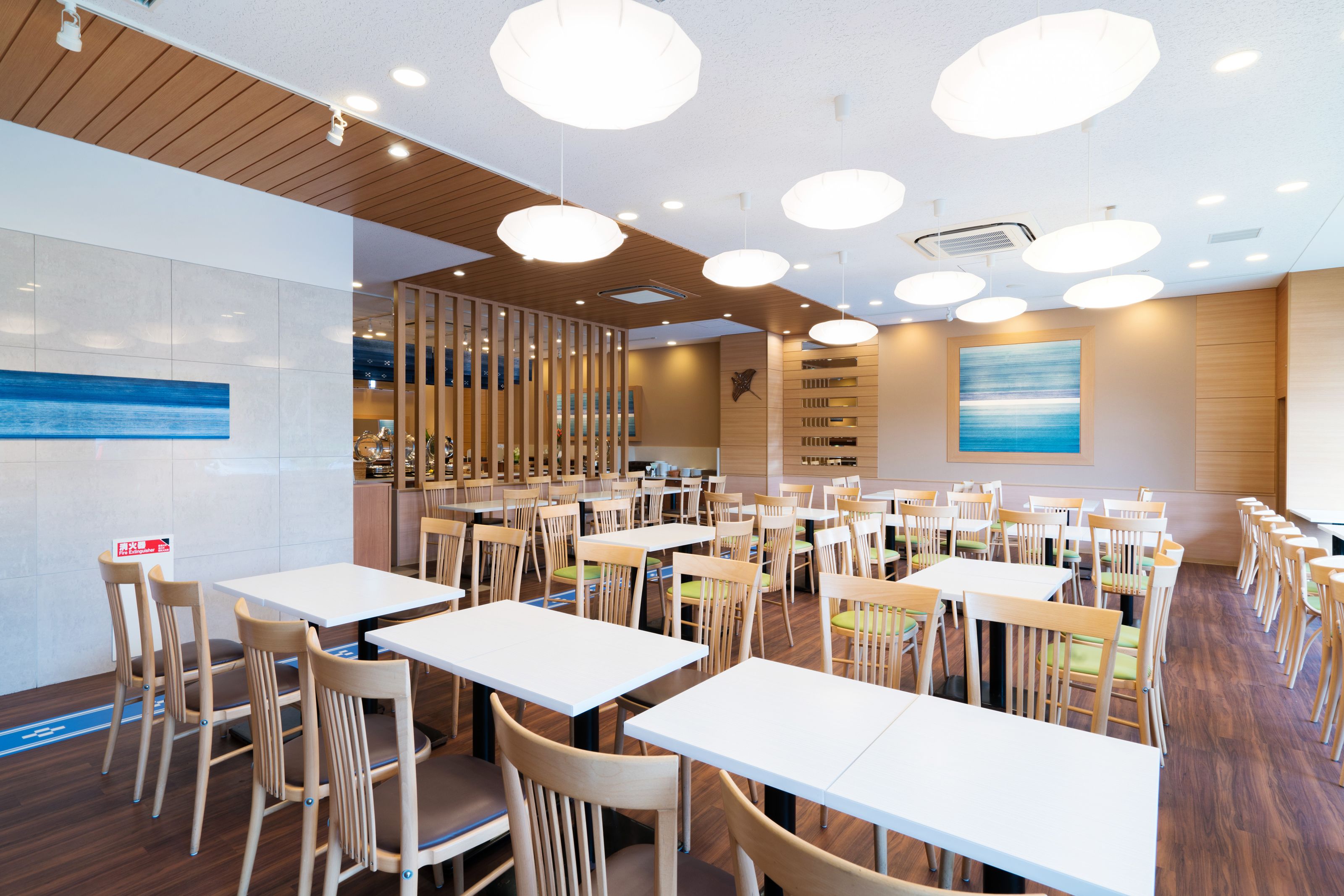 Un'ampia sala ristorante con numerosi tavoli e sedie, pannelli di legno a soffitto e lampade a sospensione.