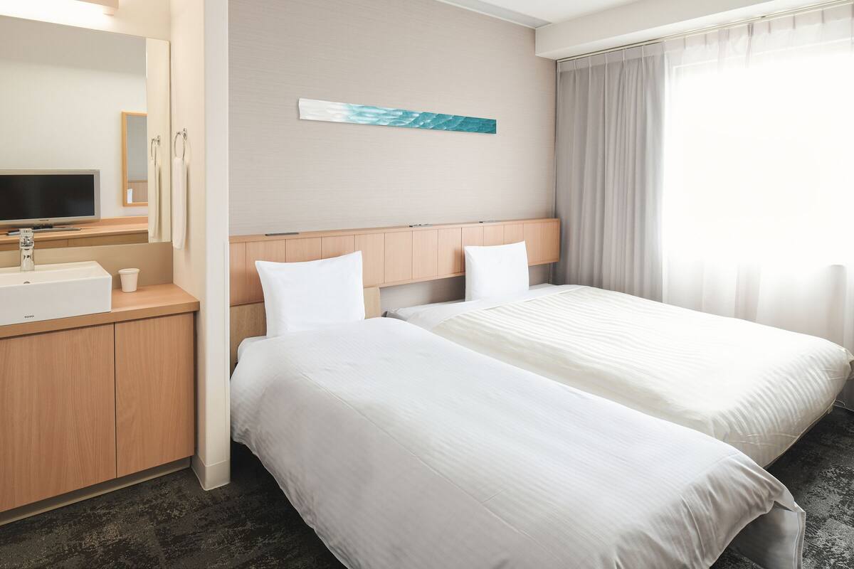 A hotel room with a bed, a TV, a sink, and a mirror.