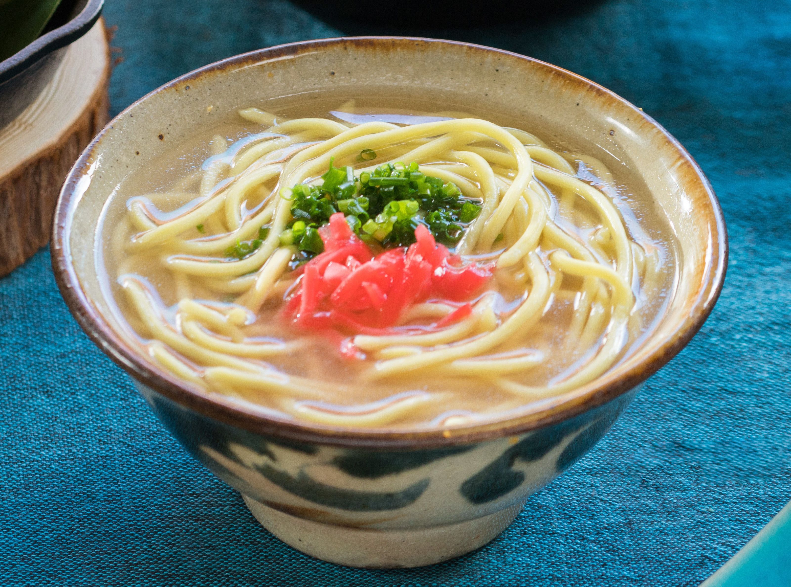 A bowl of ramen with noodles, broth, green onions, and a slice of red vegetable.