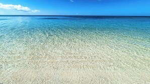 A clear view of a beach with shallow, clear water and a sandy shore under a bright blue sky.