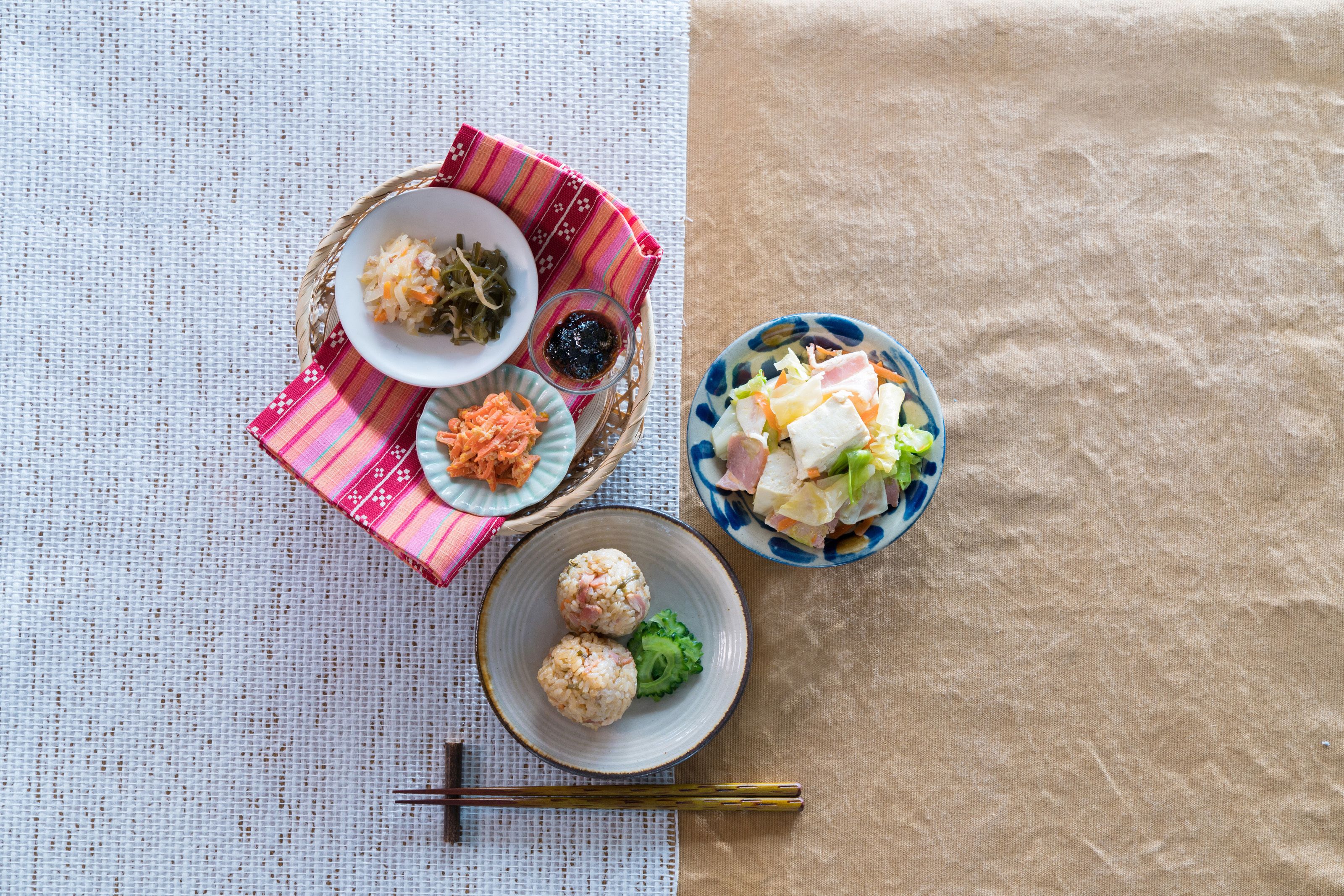 A table with various dishes, including a bowl of rice balls, a plate of vegetables, and a bowl of salad.
