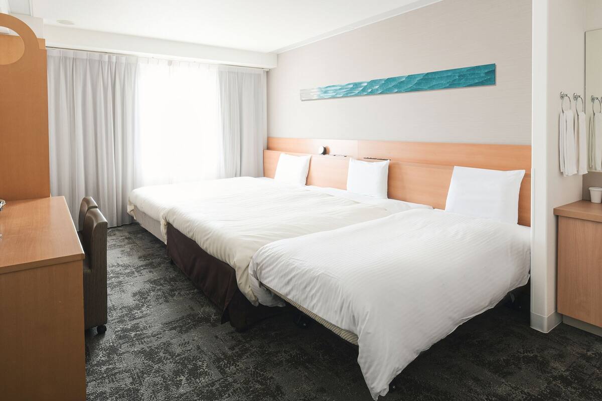 A hotel room with two beds, a desk, and a window with curtains.