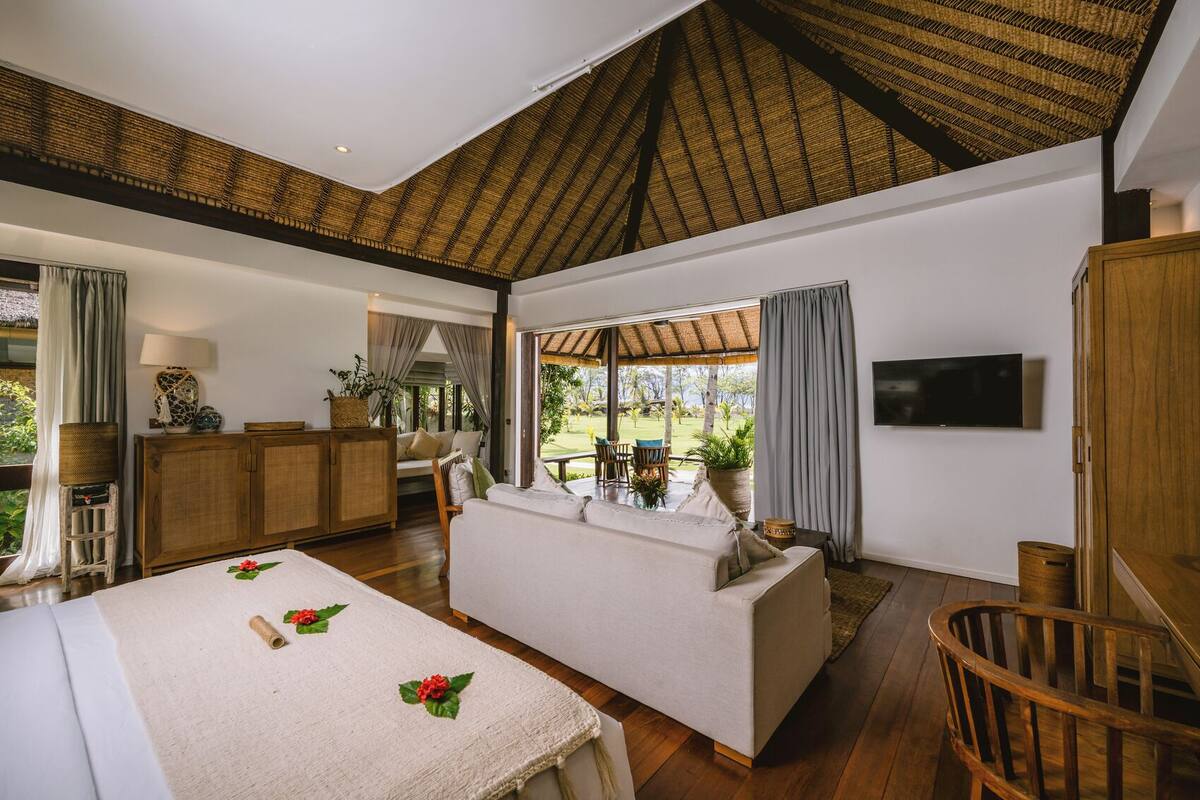 A spacious room with a large bed, a sofa, a TV, and a view of the outdoors.