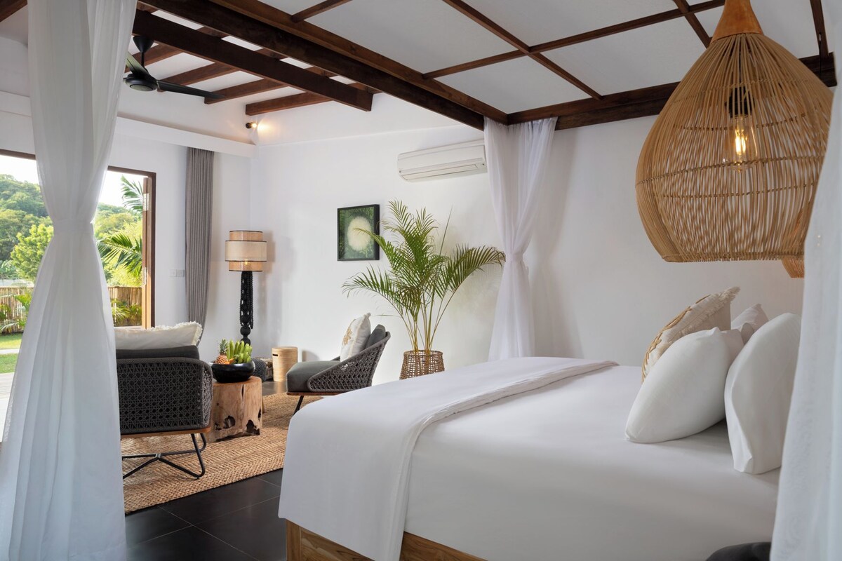 A bedroom with a bed, a chair, a lamp, a plant, and a ceiling fan.