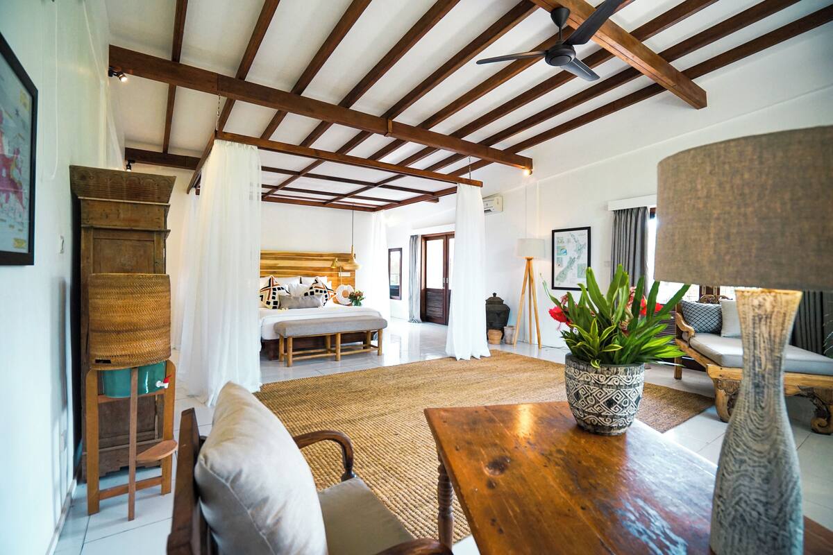 A spacious living area with a high ceiling, wooden beams, a large window, and a cozy seating arrangement.