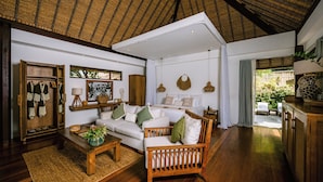 A spacious living area with a high ceiling, a wooden wardrobe, a sofa set, a coffee table, and a view of the garden.