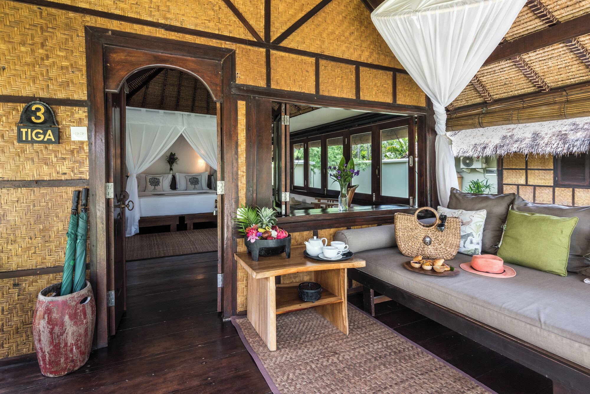 A room with a bed, a sitting area with a sofa, a table with a vase and a teapot, and a door with a number sign.