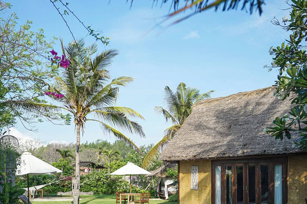A pool area with a thatched-roof building, lounge chairs, and potted plants.